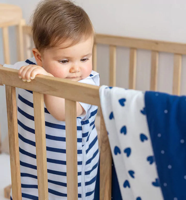 Un bébé tenant la rembarre d'un berceau | Babykare.fr