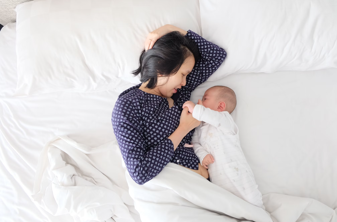 Une mère allongée sur un lit avec son bébé - Babykare.fr